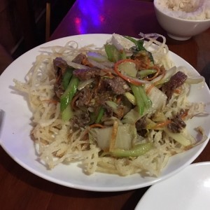 carne salteada con vegetales, sobre una cama de fideos de arroz fritos